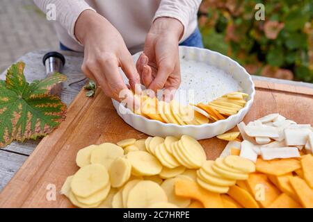 Ein Gratin aus Kartoffeln, Kürbis und Jerusalem Artischocke zubereiten, die geschnittenen Zutaten in einer gebutterten Backform anrichten Stockfoto