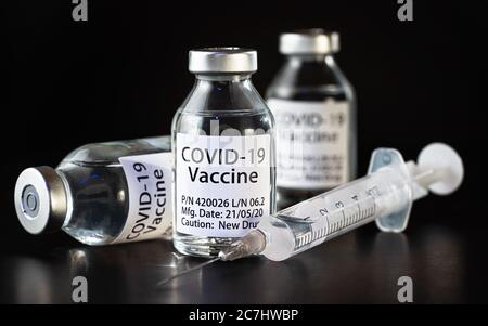 Coronavirus Covid-19 Impfstoffkonzept - drei Glasfläschchen auf schwarzem Tisch, hypodermische Spritzennadel in der Nähe, Nahaufnahme Detail (Label eigenes Design - Dummy dat Stockfoto