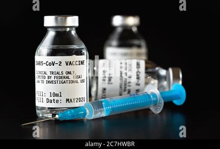 Coronavirus Covid-19 Impfstoffkonzept - drei Glasfläschchen auf schwarzem Tisch, blaue Spritzennadel in der Nähe, Nahaufnahme Detail (Label eigenes Design - dumm Stockfoto