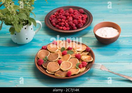 Pfannkuchen Getreide und rote reife frische Himbeeren in einem braunen Teller auf einem blauen Holztisch. Köstliches Sommerfrühstück Stockfoto