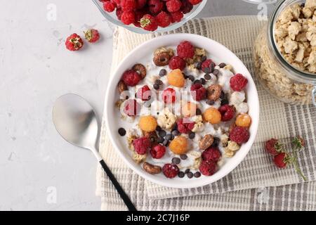 Müsli knusprig Honig Müsli mit Naturjoghurt, frische rote und gelbe Himbeeren, Schokolade und Nüsse in einer Schüssel auf grauem Hintergrund, gesunde Ernährung, Ansicht Stockfoto