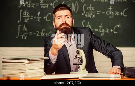 Pädagogische Gespräch. Im Gespräch mit Studenten oder Schüler. Schule Lehrer Konzept. Lehrer bärtiger Mann interessante Geschichte erzählen. Lehrer charismatische hipster Sitzen am Tisch Klassenzimmer Tafel Hintergrund. Stockfoto