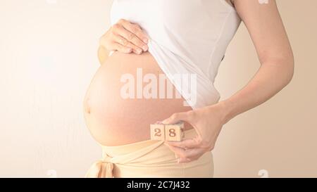 Schwangere junge Frau mit Schwangerschaft Woche Nummer neben ihrem Bauch. Fotos von Bauchwachstum bei 28 Wochen Schwangerschaft. Gesunde Schwangerschaft Ernährung Stockfoto