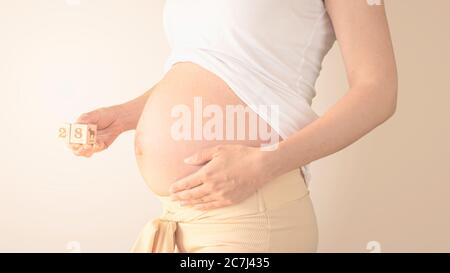 Schwangere junge Frau mit Schwangerschaft Woche Nummer neben ihrem Bauch. Fotos von Bauchwachstum bei 28 Wochen Schwangerschaft. Gesunde Schwangerschaft Ernährung Stockfoto