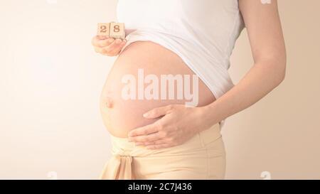 Schwangere junge Frau mit Schwangerschaft Woche Nummer neben ihrem Bauch. Fotos von Bauchwachstum bei 28 Wochen Schwangerschaft. Gesunde Schwangerschaft Ernährung Stockfoto