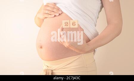 Schwangere junge Frau mit Schwangerschaft Woche Nummer neben ihrem Bauch. Fotos von Bauchwachstum bei 26 Wochen Schwangerschaft. Gesunde Schwangerschaft Ernährung Stockfoto