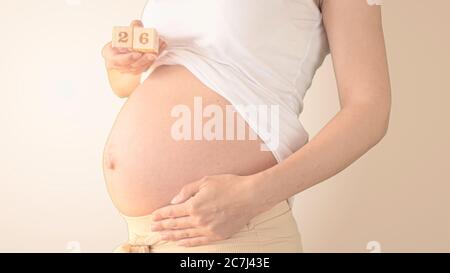 Schwangere junge Frau mit Schwangerschaft Woche Nummer neben ihrem Bauch. Fotos von Bauchwachstum bei 26 Wochen Schwangerschaft. Gesunde Schwangerschaft Ernährung Stockfoto