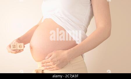Schwangere junge Frau mit Schwangerschaft Woche Nummer neben ihrem Bauch. Fotos von Bauchwachstum bei 26 Wochen Schwangerschaft. Gesunde Schwangerschaft Ernährung Stockfoto