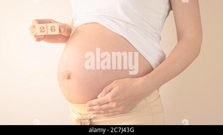 Schwangere junge Frau mit Schwangerschaft Woche Nummer neben ihrem Bauch. Fotos von Bauchwachstum bei 26 Wochen Schwangerschaft. Gesunde Schwangerschaft Ernährung Stockfoto