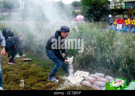 Die Einheimischen werfen Mehlbomben auf die Flofts, die am jährlichen ‘Ouseday’ Lewes to Newhaven Raft Race auf dem River Ouse, Lewes, Sussex, Großbritannien, teilnehmen Stockfoto