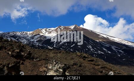 Ätna, Nationalpark Ätna, Parco dell –´Ätna, schneebedeckter Gipfel des Ätna, brauner Lavahang im Vordergrund, dunkelblauer Himmel, weiße Wolken Stockfoto