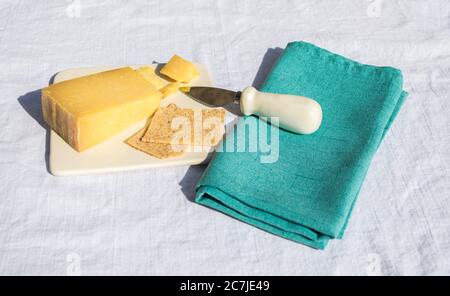 Ein Keil Cheddar-Käse und zwei Cracker auf einem Käseplatte mit einem kleinen Messer auf einer grünen Leinenserviette bei einem Picknick Stockfoto