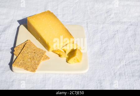 Ein Keil Cheddar-Käse und zwei Cracker auf einem Käseplatte auf einem weißen Leinentischtuch bei einem Picknick mit Kopierplatz Stockfoto