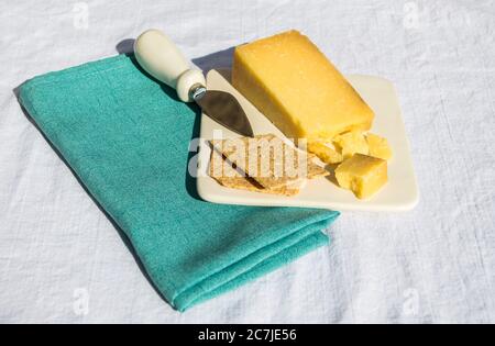Ein Keil Cheddar-Käse und zwei Cracker auf einem Käseplatte mit einem kleinen Messer auf einer grünen Leinenserviette bei einem Picknick Stockfoto