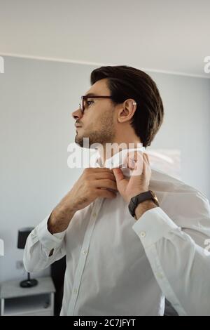 Junge attraktive Brünette Mann in weißem Hemd und Brille nachdenklich Blick beiseite zu Hause Stockfoto