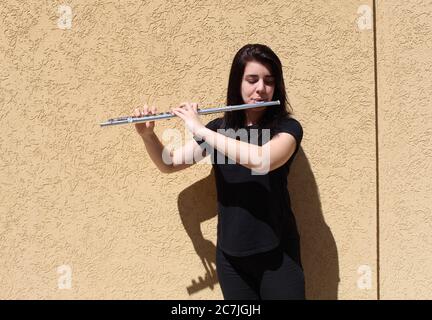 Das schwarzhaarige Mädchen spielt draußen vor einer Wand die Flöte Stockfoto