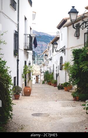 Allee mit Blumentöpfen entlang der weiß getünchten Häuser mit Blick auf die Berge in der Altstadt von Altea, Costa Blanca, Spanien Stockfoto