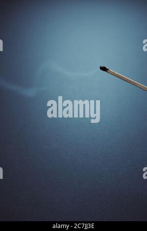 Vertikale Aufnahme eines verbrannten Streichholzstachel mit einer blauen Wand Im Hintergrund Stockfoto