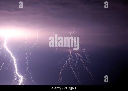 Viele helle Blitze entlädt sich im stürmischen Himmel unter schweren purpurnen Regenwolken Stockfoto