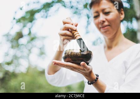 Junge lächelnde Frau spielt auf Messing tibetischen Klangschale draußen. Klangtherapie und Meditation Stockfoto