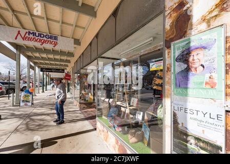 Ein Plakat in einer Zeitschrift vor einer Nachrichtenagentur von Königin Elizabeth II scheint zu beobachten, wie ein älterer Mann mit seiner Morgenzeitung den Laden verlässt. Stockfoto