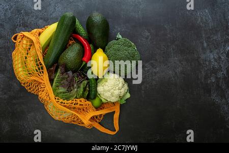 Reifes Gemüse und Früchte in einem orangefarbenen Saitenbeutel auf dunklem Hintergrund. Stockfoto