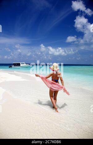 Junge Frau, die auf den Malediven am menschenleeren weißen Sandstrand entlang geht, umgeben von tropischen Gewässern Stockfoto