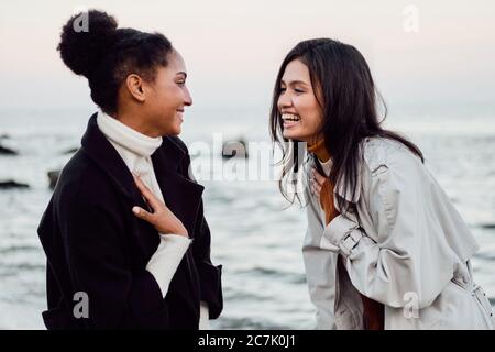 Zwei fröhliche Mädchen, die sich gerne unterhalten und gemeinsam am Meer spazieren gehen