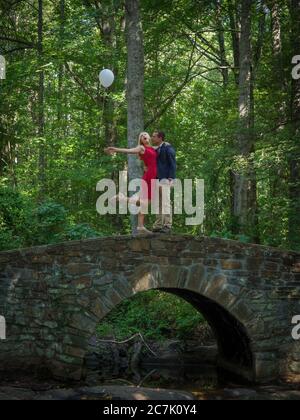 Paar mit weißen Ballons stehen auf einer Brücke umgeben von Grün in einem Wald Stockfoto