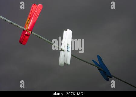 Drei bunte Wäscheklammern hängen an einem Seil mit einem dunklen Hintergrund Stockfoto