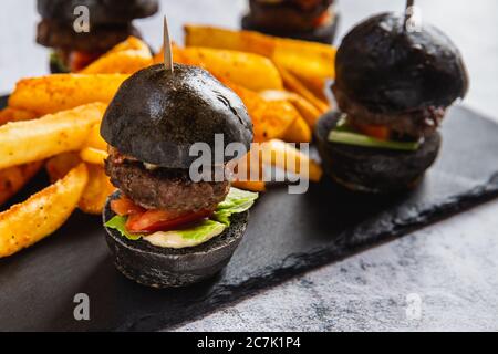 Leckere Mini-Burger mit Rindfleisch, Tomaten, Käse serviert mit pommes auf schwarzem Tisch Stockfoto