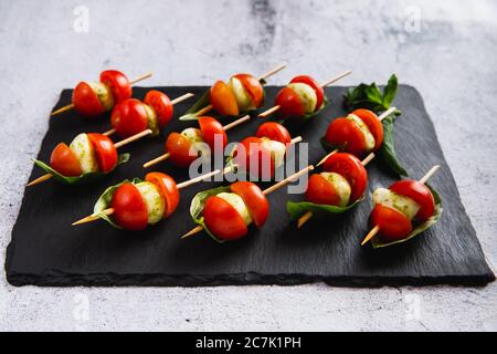 Kleine Snacks kandieren mit Kirschtomaten, Mozzarella auf Spieß auf einem schwarzen Schieferteller. Stockfoto