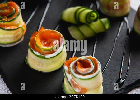 Nahaufnahme der Zucchini-Brötchen mit Lachs und weicher Käsecreme auf schwarzem Teller Stockfoto