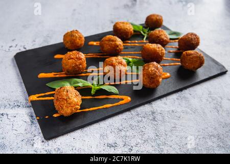 Gebratene Kartoffelkäsekugeln oder Kroketten mit Orangensauce und grünem Salat. Selektiver Fokus Stockfoto