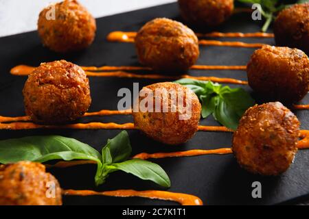 Gebratene Kartoffelkäsekugeln oder Kroketten mit Orangensauce und grünem Salat. Selektiver Fokus Stockfoto