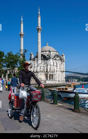 Ein Mann fährt an der wunderschön gestalteten Ortakoy Camii (Moschee) vorbei, die neben dem Bosporus in Ortakoy in Istanbul in der Türkei liegt. Stockfoto