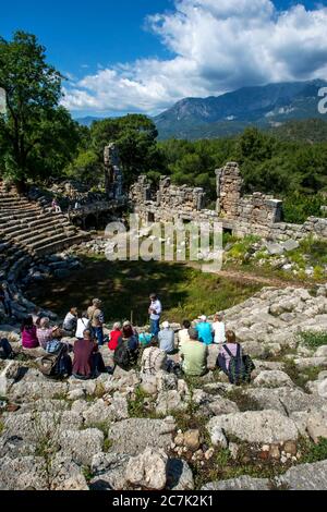 Touristen sitzen unter den Ruinen des Theaters in der antiken griechischen und römischen Stadt Phaselis in Kemer in der Türkei, die aus dem Jahr 700 v. Chr. stammt. Stockfoto