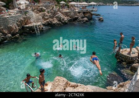 Schwimmer tauchen an einem heißen Sommertag am Felsstrand in Kas an der türkischen Mittelmeerküste gerne ins Meer. Stockfoto