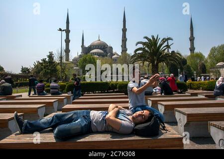 Männer entspannen sich auf Parkbänken im Sultanahmet Park in Istanbul in der Türkei. Im Hintergrund steht die prächtige Blaue Moschee (Sultan Ahmet Camii). Stockfoto