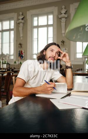 Junge attraktive männliche Student mit Büchern träumen, während das Studium in der Bibliothek der Universität Stockfoto