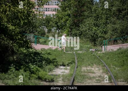 Bukarest / Rumänien - 14. Juli 2020: Alte Frau geht mit ihrem Hund über eine alte verlassene Eisenbahn zwischen schwerer Vegetation in der Stadt. Stockfoto