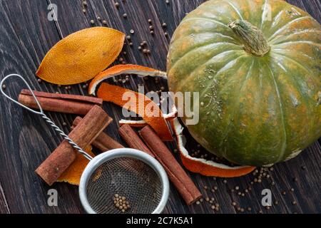 Zimt, Orangenkrusten, Gewürze, Metallsieb und reifer Kürbis auf einem Holztisch Stockfoto