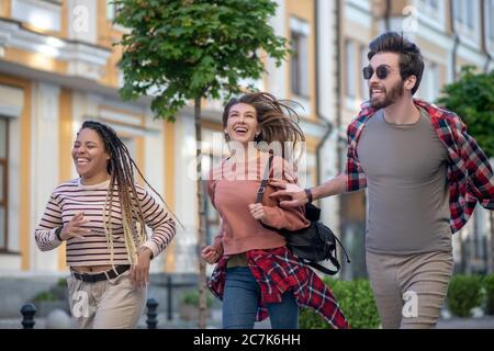 Kerl in Sonnenbrille und zwei langhaarige Mädchen laufen vorwärts Stockfoto