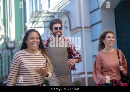 Mann in Sonnenbrille und zwei Mädchen, die die Straße hinunter laufen Stockfoto