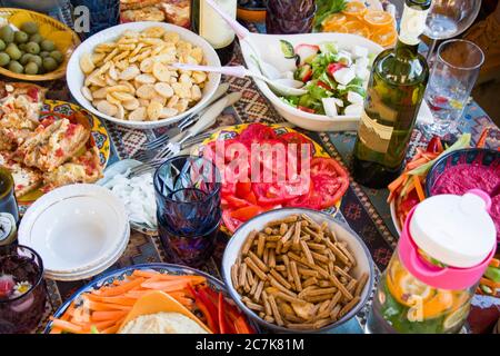 Volle Tischansicht, Tomaten, Snacks, Wein, Wasser mit Zitrone und Minze, Salat, Pizza und andere Speisen auf dem Tisch für Party und Familie essen. Stockfoto