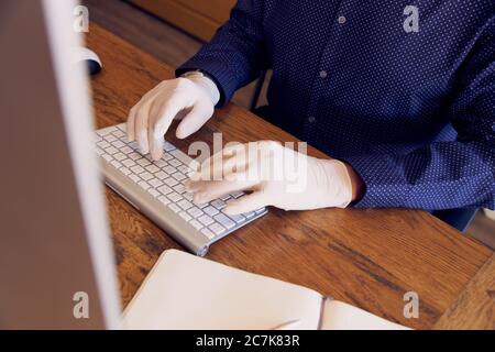 Anonymer Geschäftsmann, der am Schreibtisch arbeitet und Schutzhandschuhe trägt, die auf der Tastatur tippen. Stockfoto