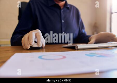Anonymer Geschäftsmann, der am Schreibtisch arbeitet und Schutzhandschuhe trägt, die auf der Tastatur tippen. Stockfoto