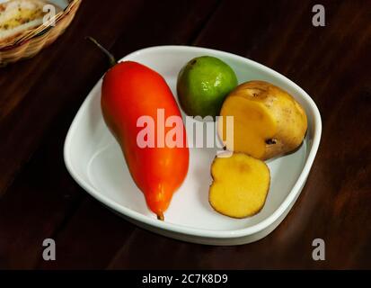 Typische Lebensmittel und Zutaten aus Peru. Gelbe Kartoffel (Papa Amarilla), eine sehr beliebte Kartoffel, Orangenpfeffer (Aji amarillo) und Limette auf einem dunklen Holz Stockfoto