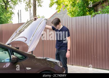 Junger Mann schaut unter die Motorhaube eines Autos in Ratlosigkeit. Auto Zusammenbruch Stockfoto