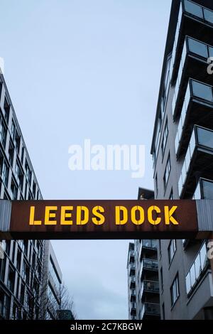 LEEDS, VEREINIGTES KÖNIGREICH - Jan 11, 2020: Vertikale Aufnahme eines Leeds Dock-Schild beleuchtet in einer bewölkten Dämmerung Nacht mit Wohnblöcken auf beiden Seiten Stockfoto